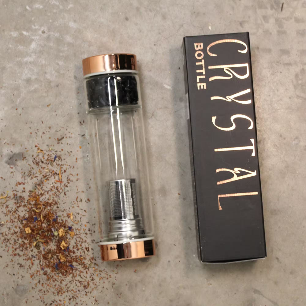 Clear crystal bottle with rose gold cap and black box labeled 'Crystal Bottle' on a textured surface.