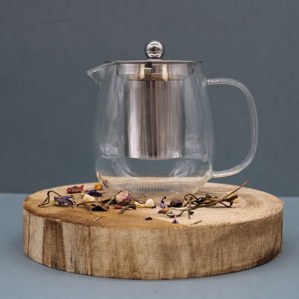 Clear glass teapot with metal lid on a wooden coaster against a gray background