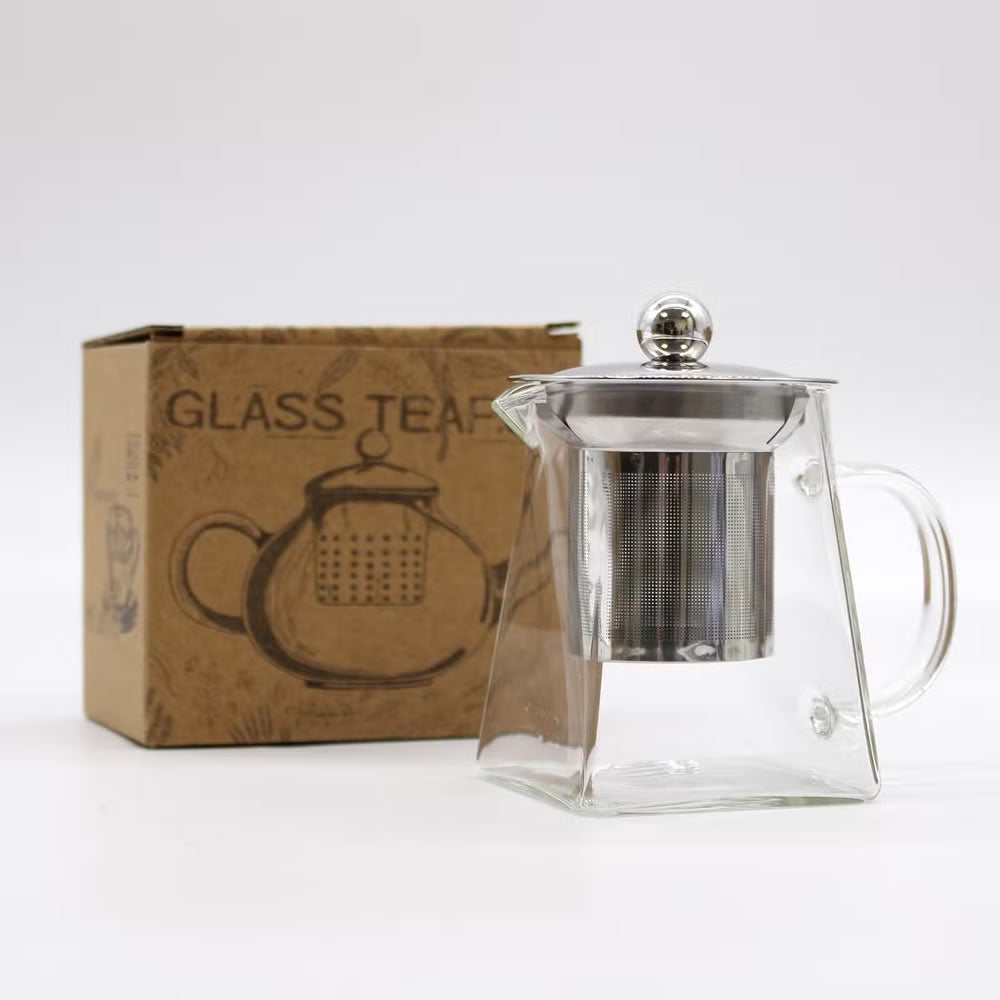 Clear glass teapot with metal lid and tea infuser on a white background, next to a cardboard box labeled 'Glass Tea'.