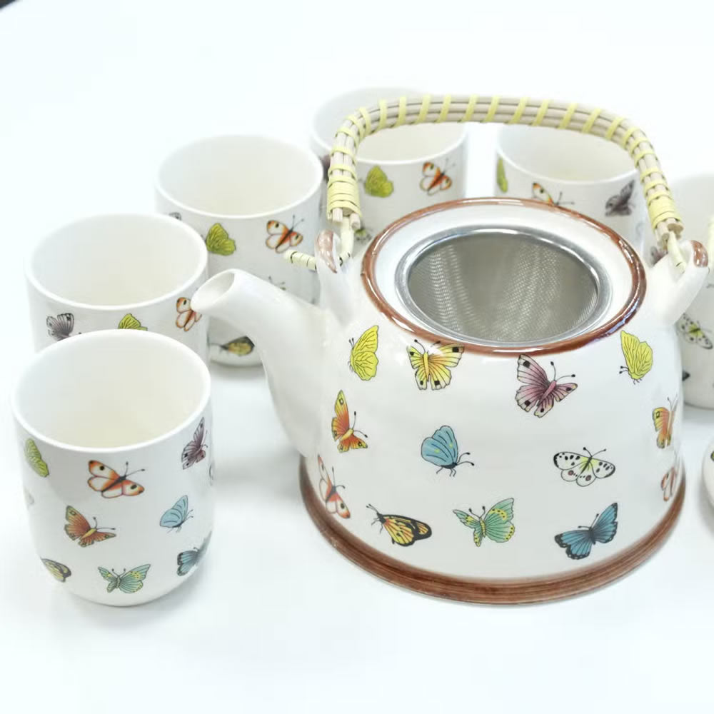 Ceramic teapot and cups with butterfly designs on a white background