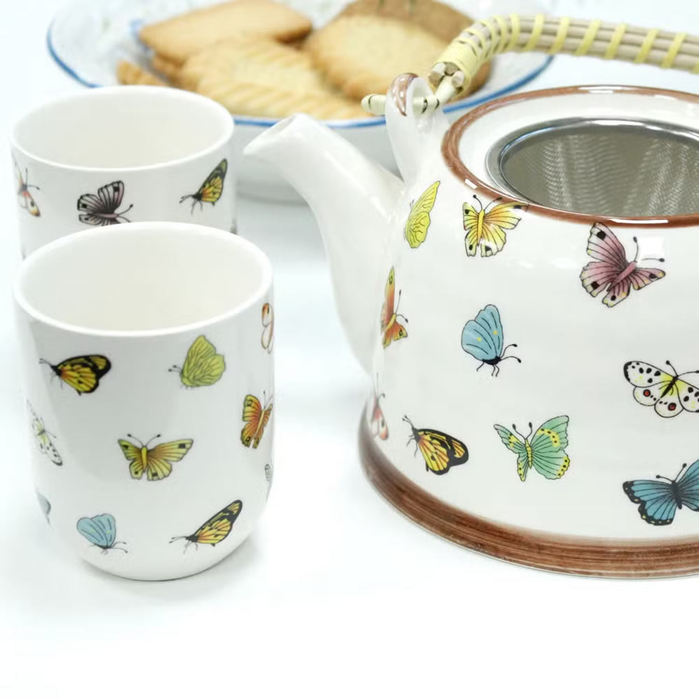 Ceramic teapot and cups with butterfly designs on a white surface.