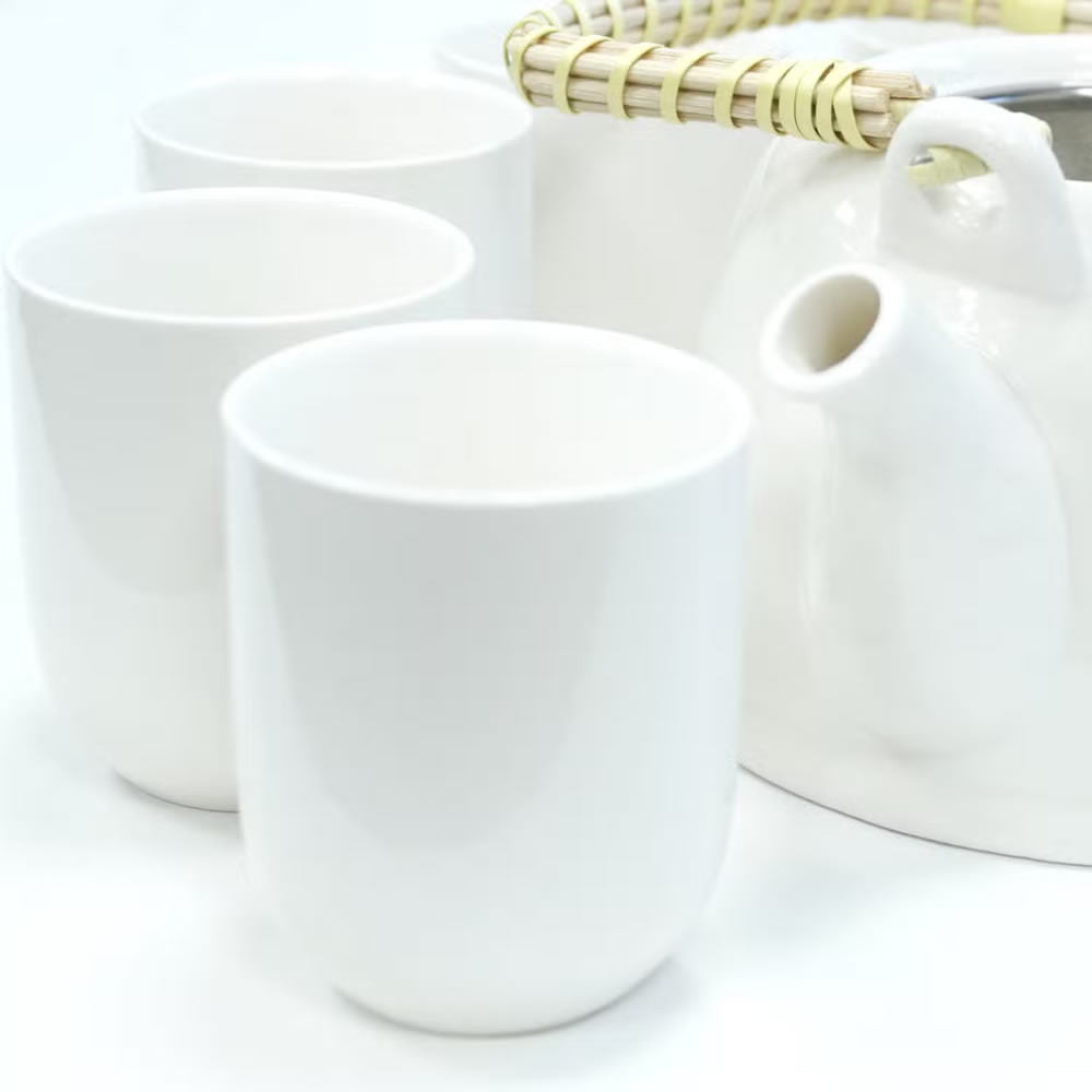 Set of white ceramic cups and a teapot on a light background