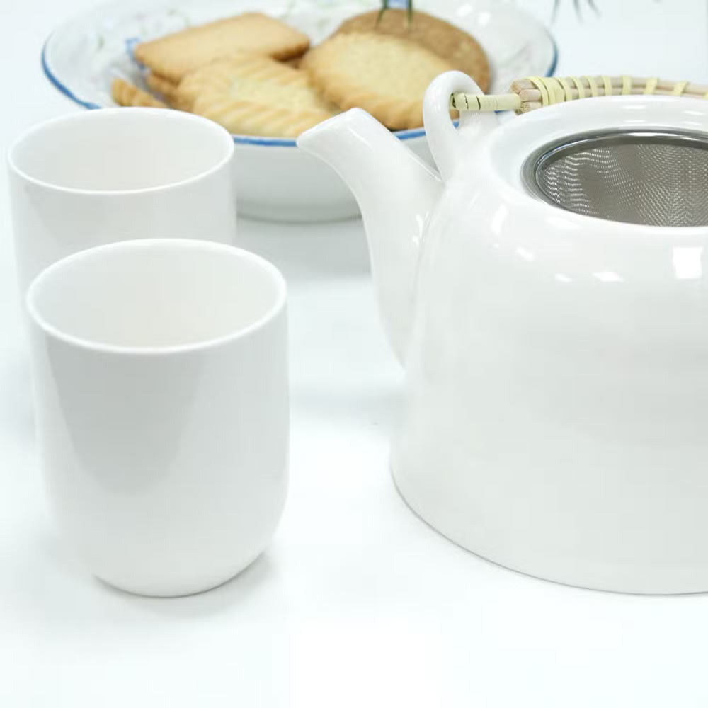 White teapot and cups with a plate of cookies on a white background