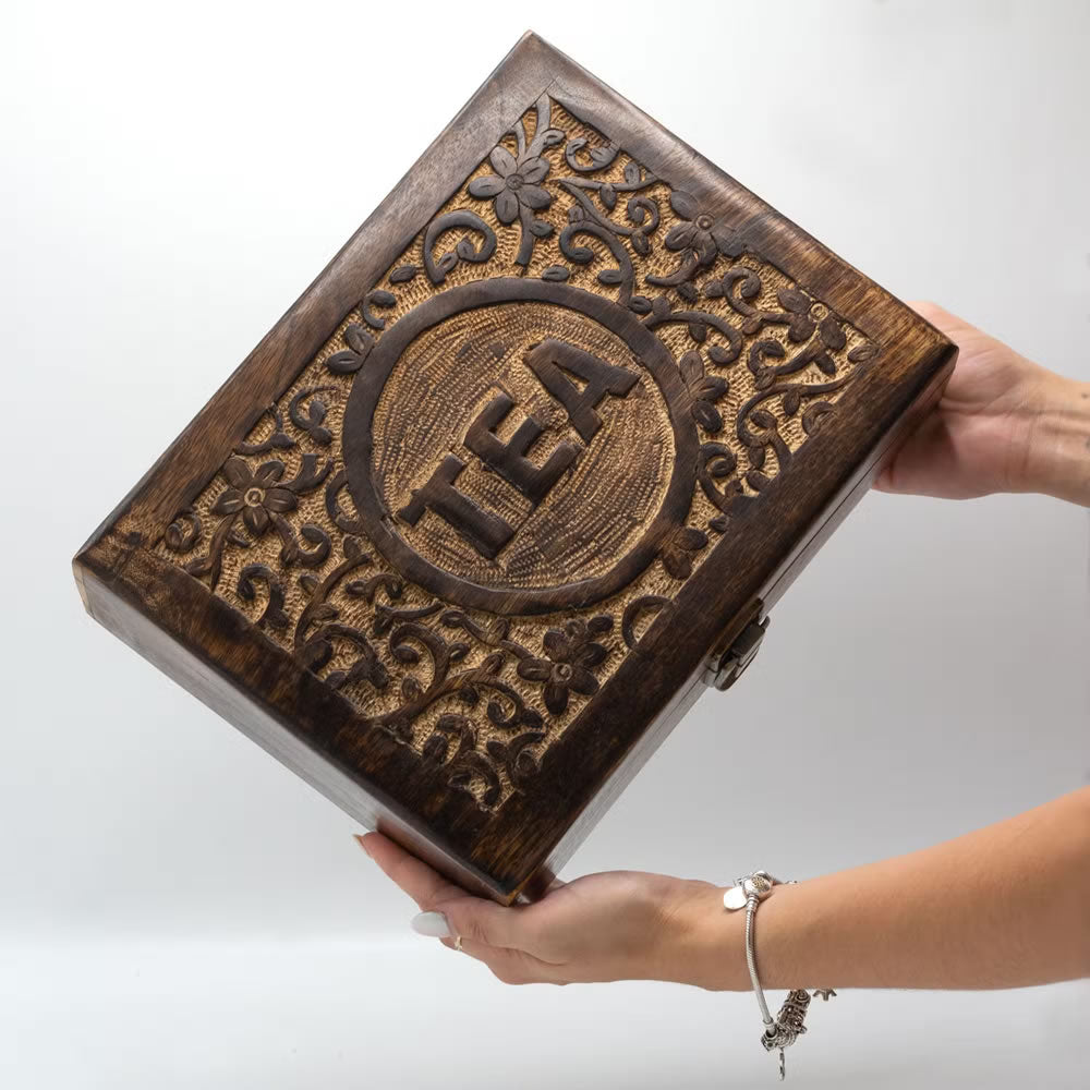 Wooden tea box with intricate carvings and 'TEA' engraving held by a hand on a white background