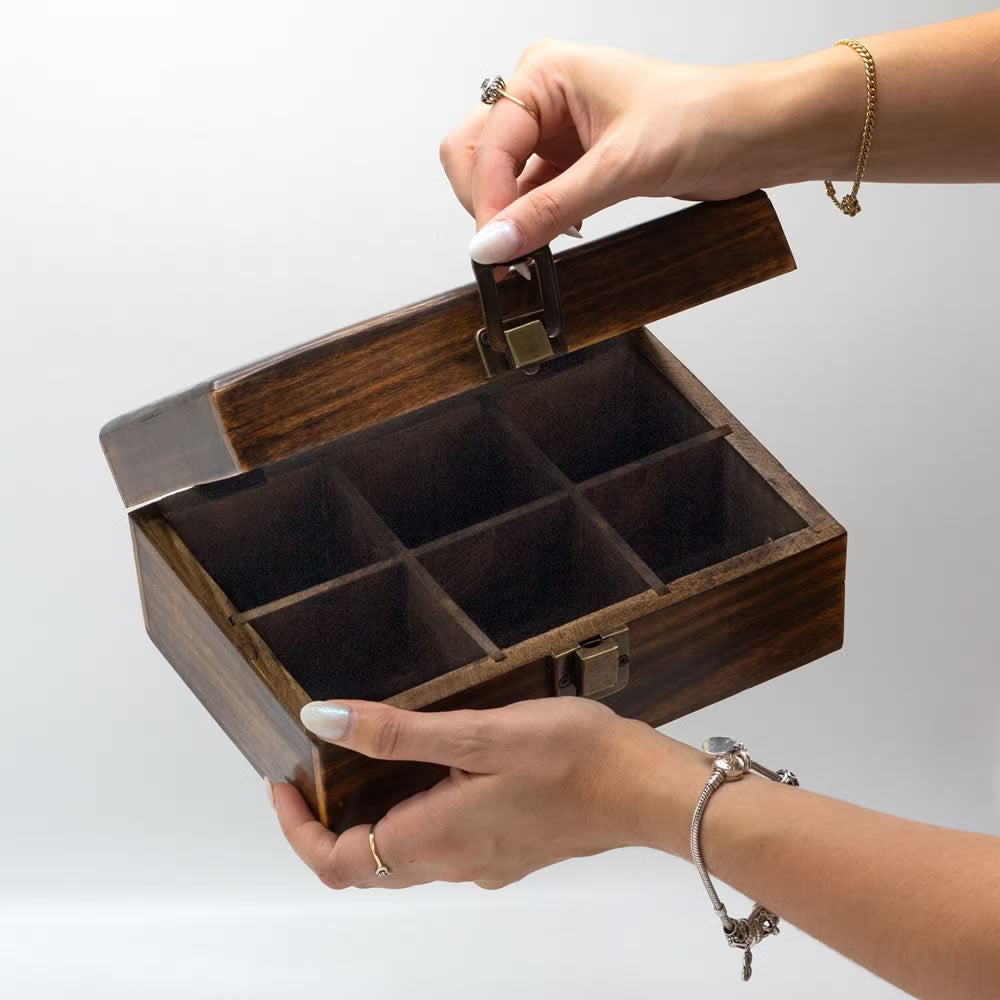 Wooden jewelry box with compartments held open by a hand on a light gray background