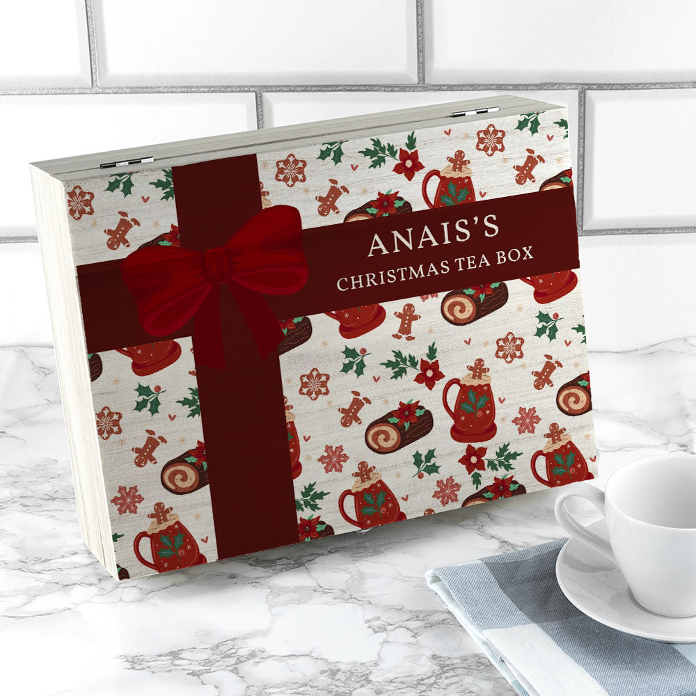 Christmas-themed tea box with a red ribbon on a marble surface with a cup and saucer.