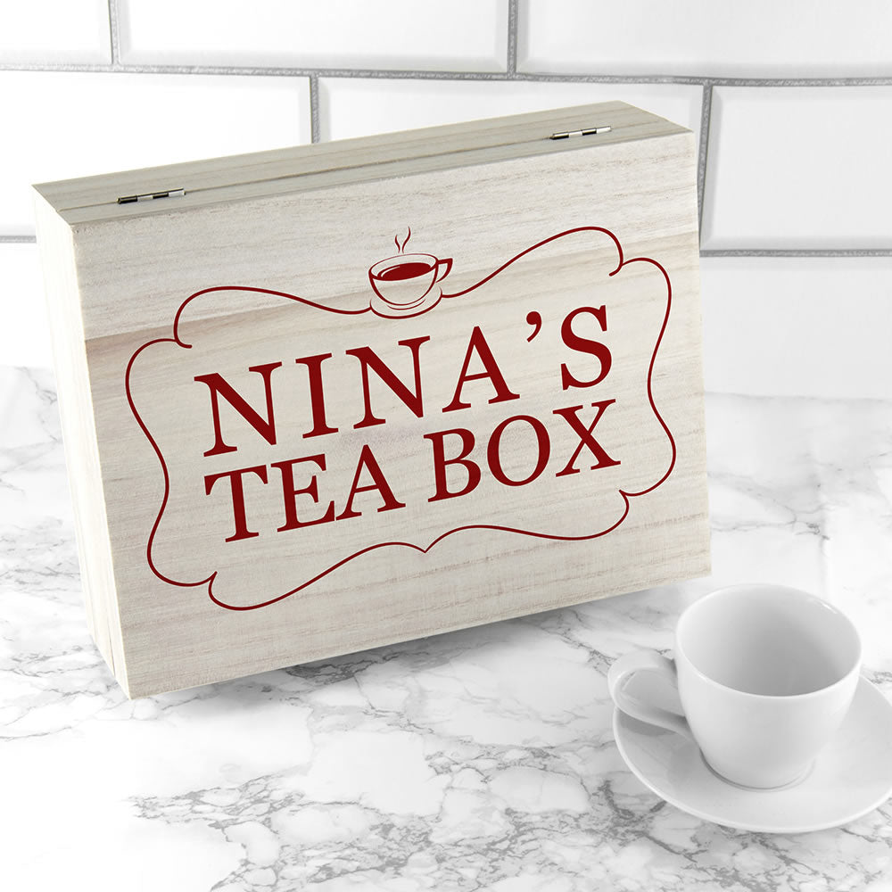Wooden tea box with 'NINA'S TEA BOX' text on a marble surface with a white cup and saucer.